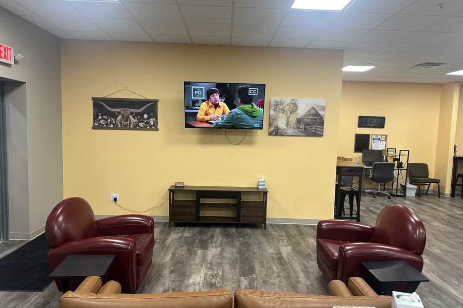 A common room with leather armchairs, a couch, and a wall-mounted television on a warm yellow wall.