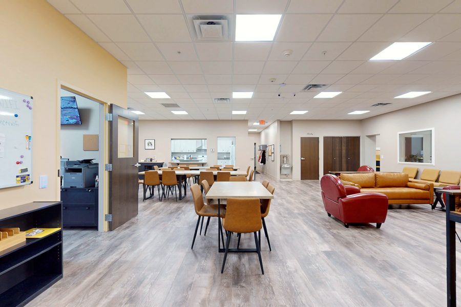 The Homeward Bound day center: dining tables and chairs on one side, soft armchairs and a couch on the other, under bright ceiling lights.