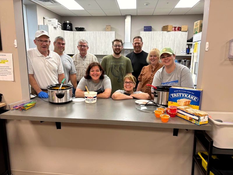 A group of eight volunteers gathered around the serving counter with slow cookers and desserts ready for dinner.