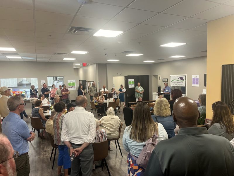 A full room of visitors seated and standing in the day center during a community open house.