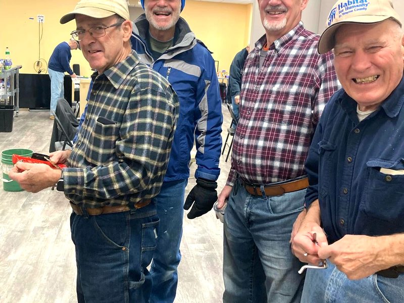Four volunteers in work clothes and caps laughing together during a build day at the shelter.