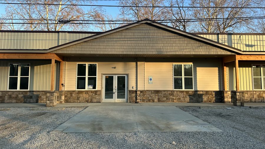 The finished shelter: cream siding, a stone base, timber porch posts, and glass double doors under a shingled gable.