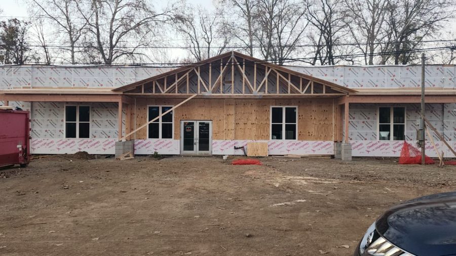 The same building mid-renovation, wrapped in housewrap with a newly framed timber gable and entrance over bare ground.