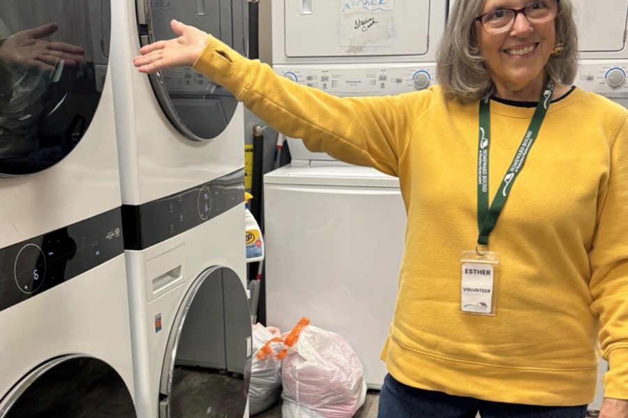 A Homeward Bound volunteer smiling beside the shelter's stacked washer and dryer units in the laundry room.