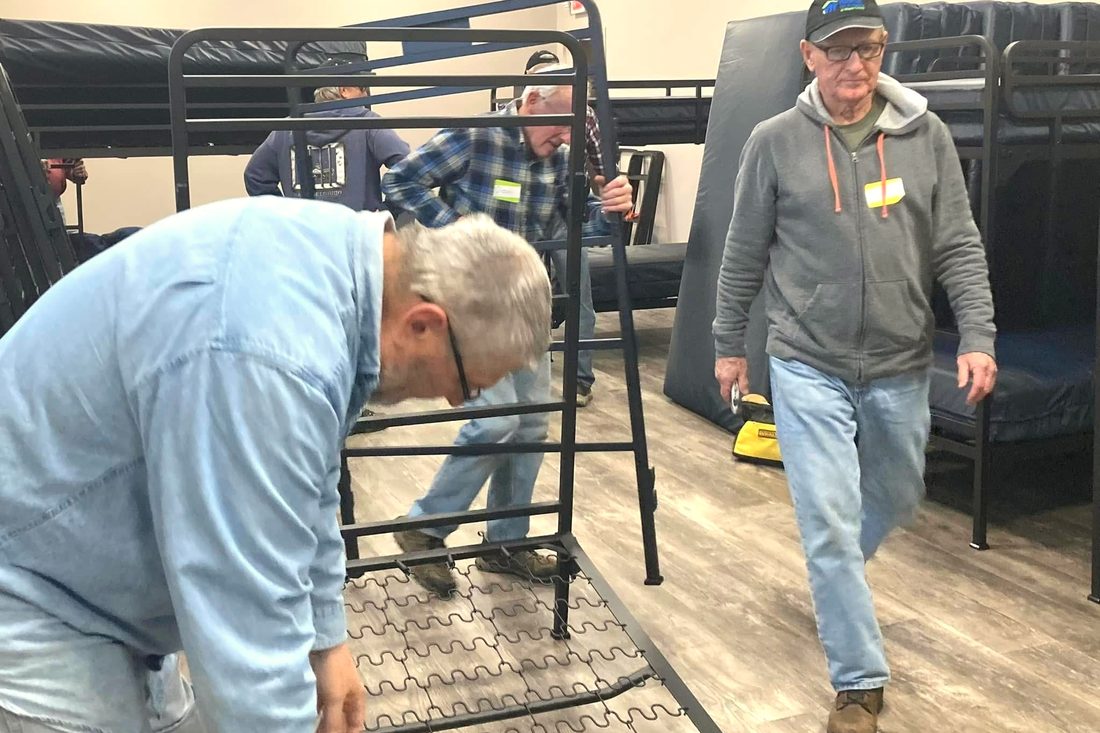 Volunteers assembling metal bunk bed frames on the floor of a sleeping room before the shelter opened.