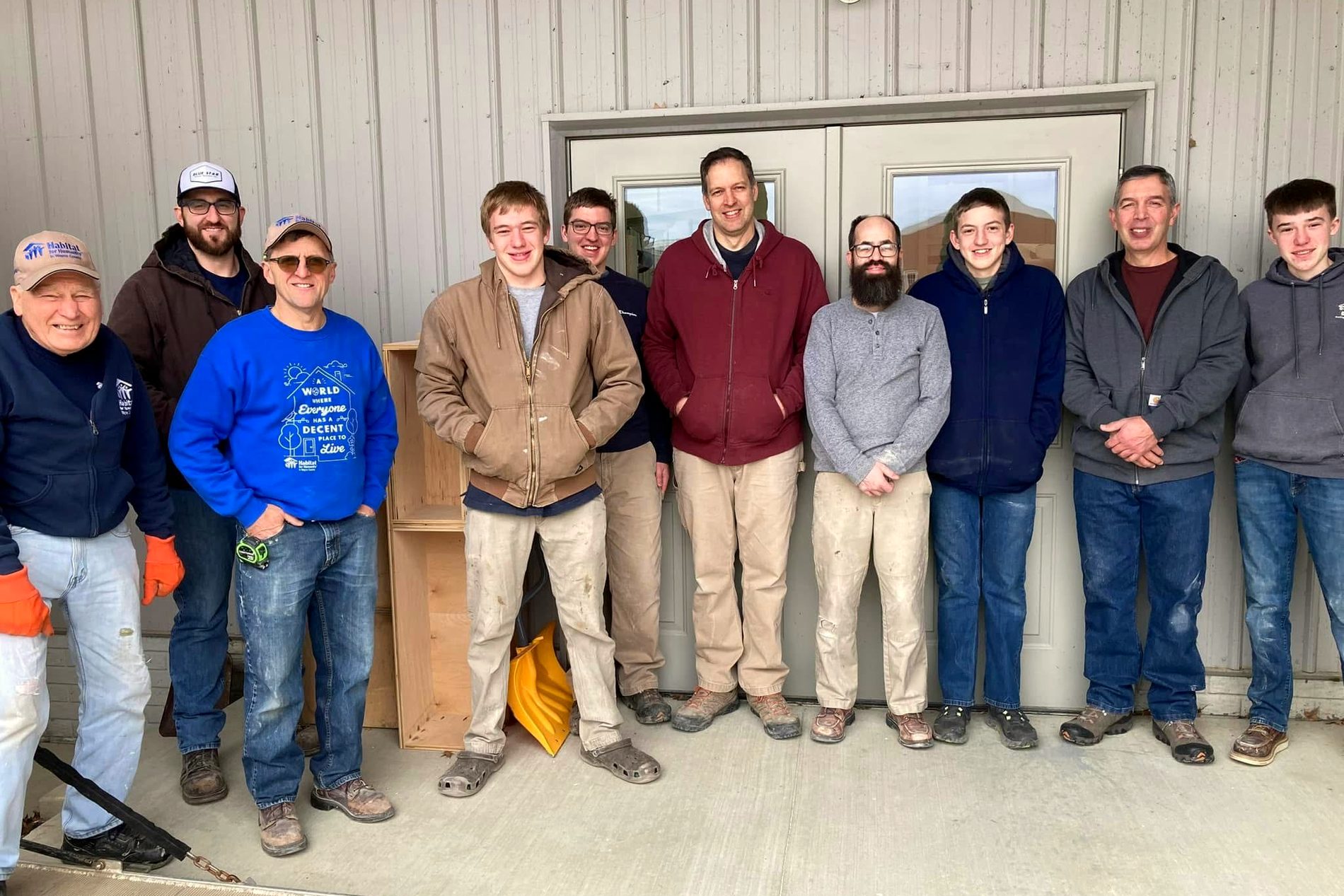 A line of eleven volunteers in coats and work clothes standing shoulder to shoulder outside the shelter after a work day.