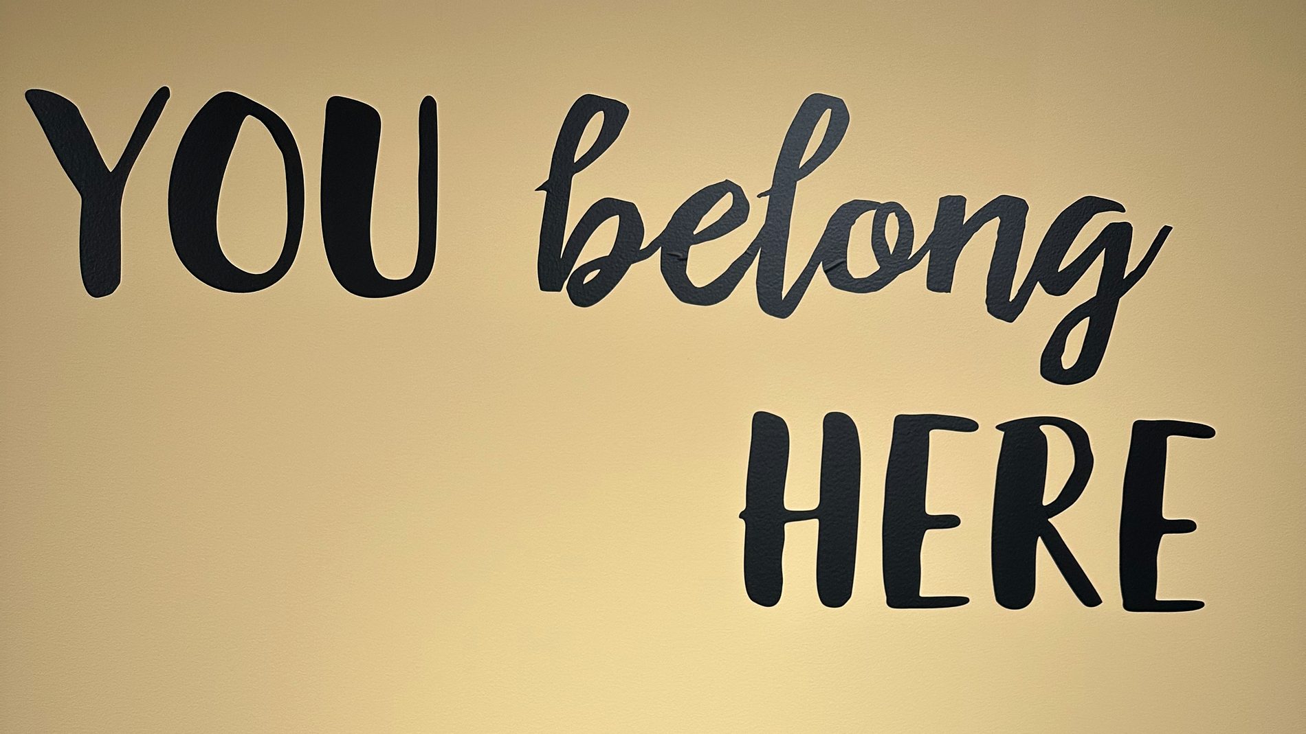Hand-painted lettering on a warm yellow wall inside the day center reading "You belong here."